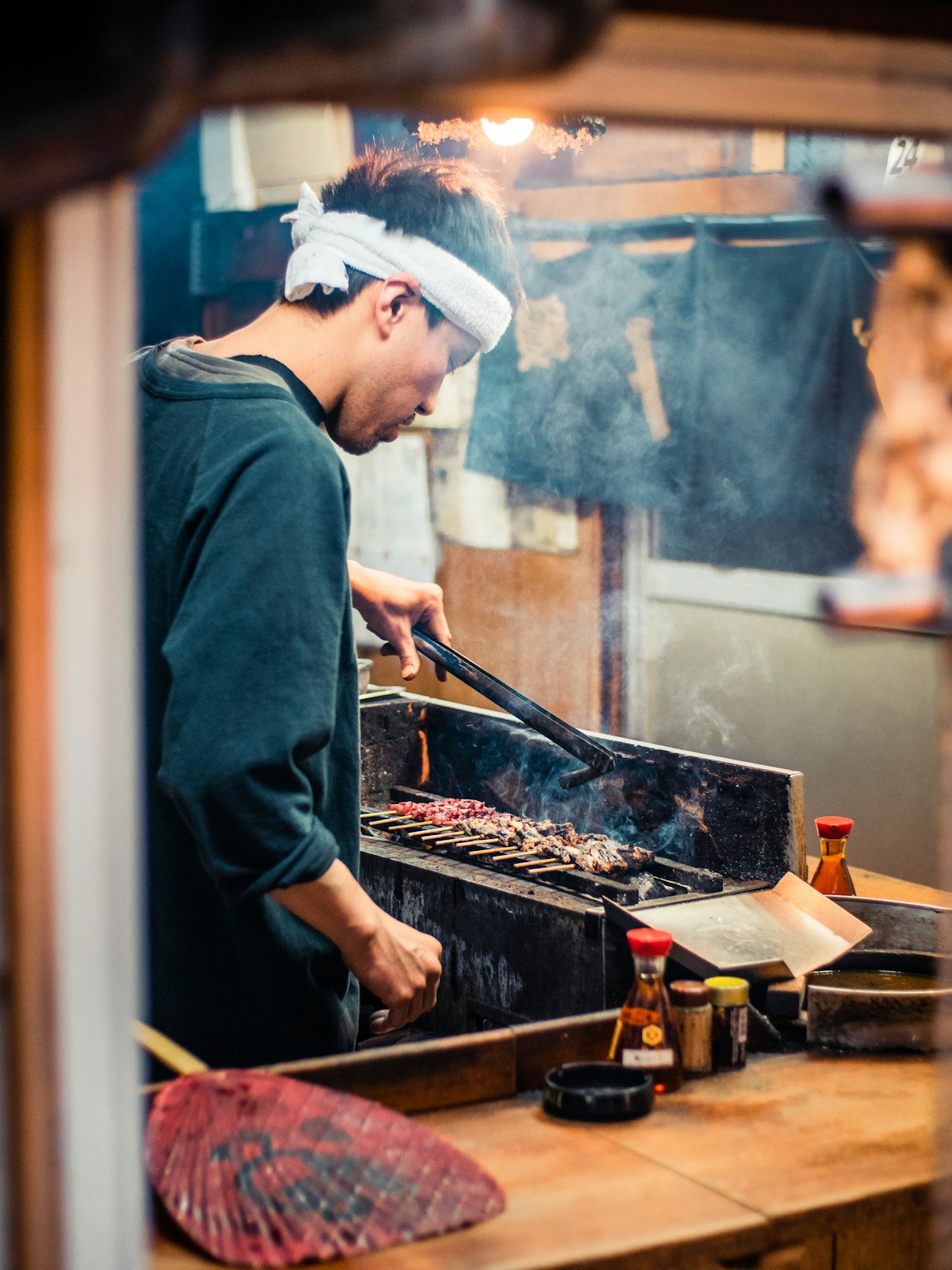 A cook grilling pork over charcoal behind the bar