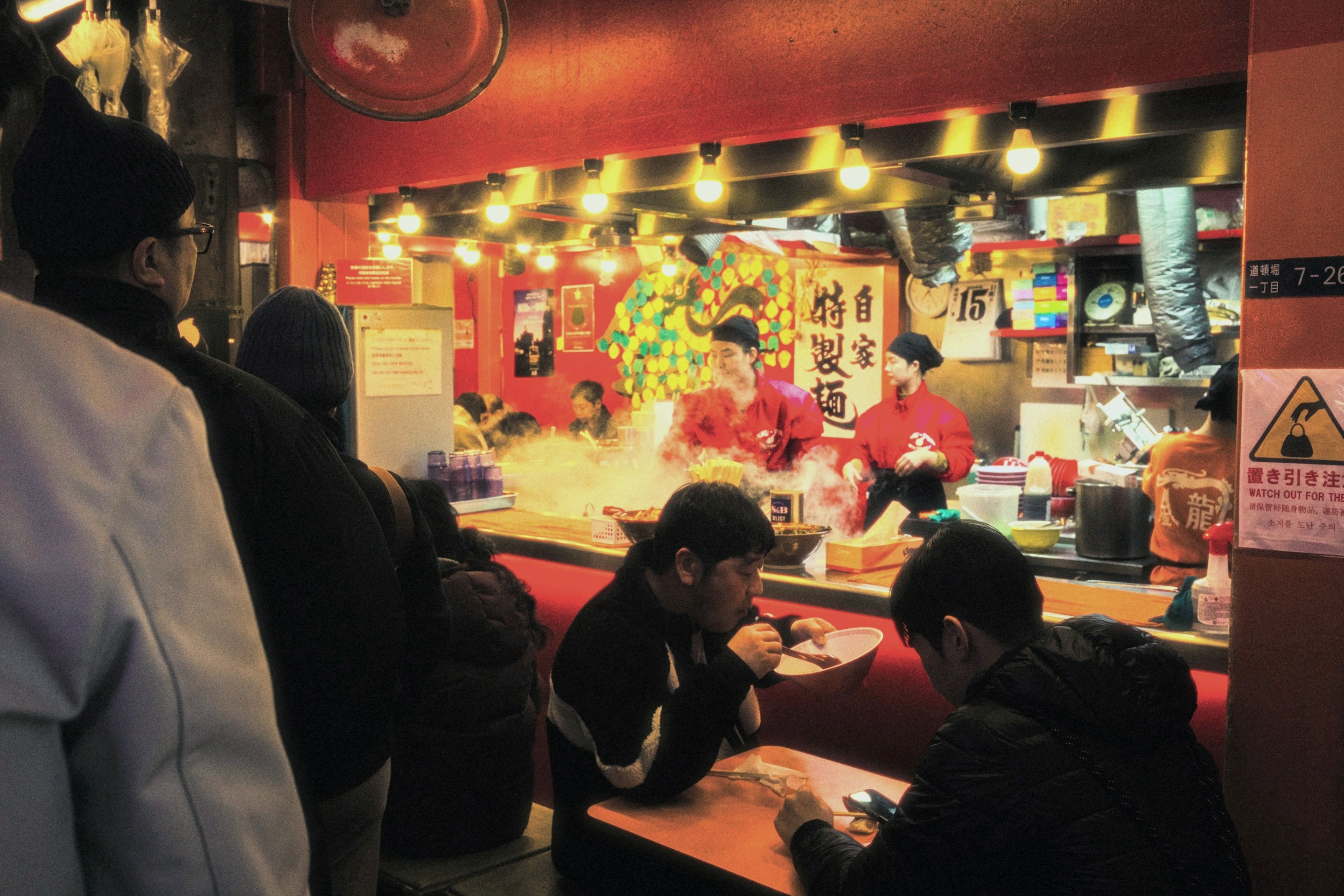 A busy ramen counter late at night, cooks working under warm lanterns while guests eat