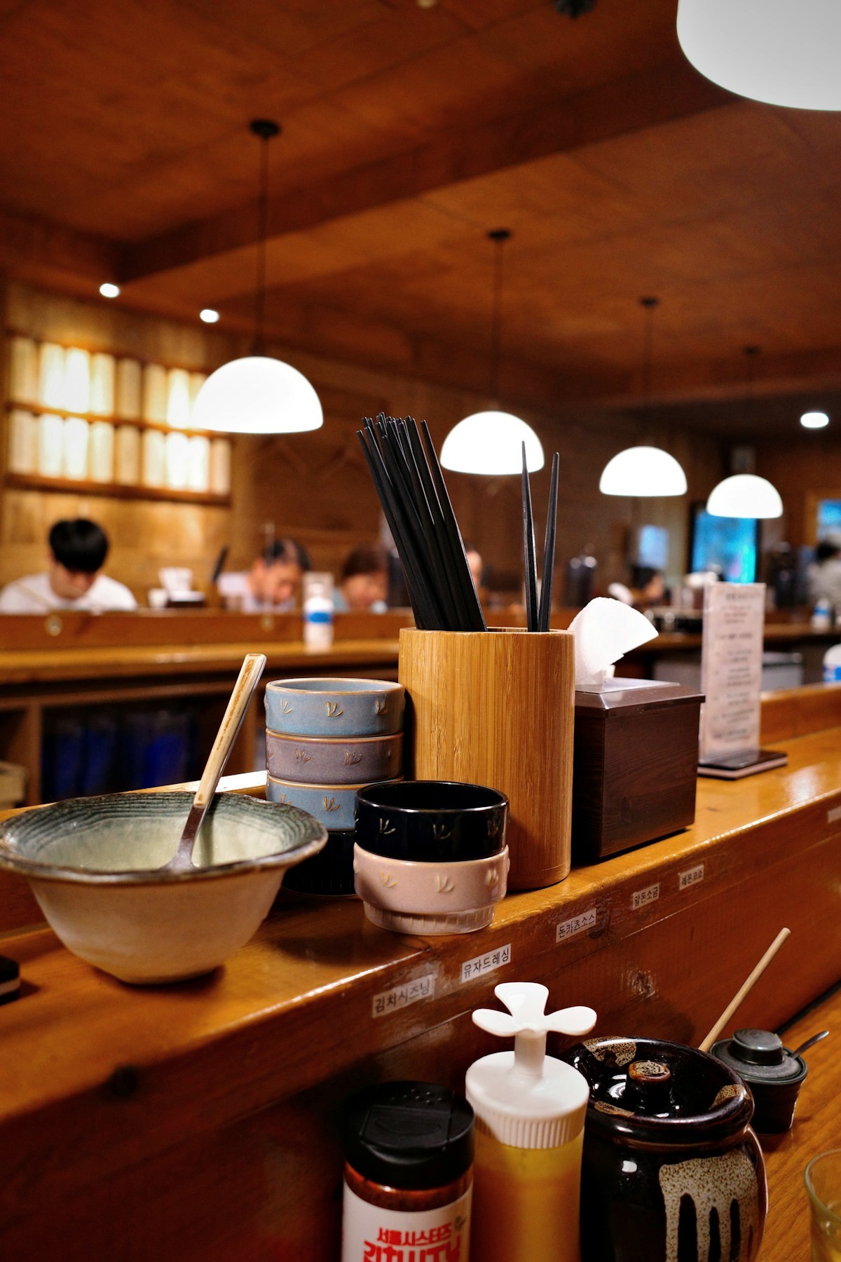 The wooden counter set with bowls, chopsticks and condiments under hanging lamps