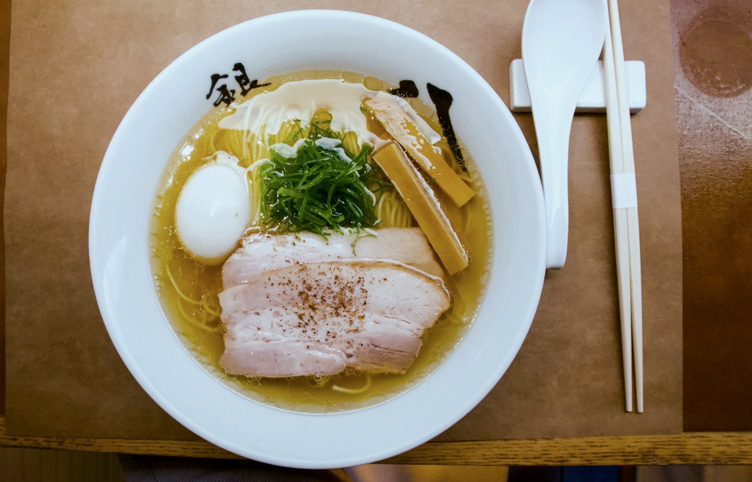 Tonkotsu from above: golden broth, chashu pork, a soft egg and greens in a white bowl