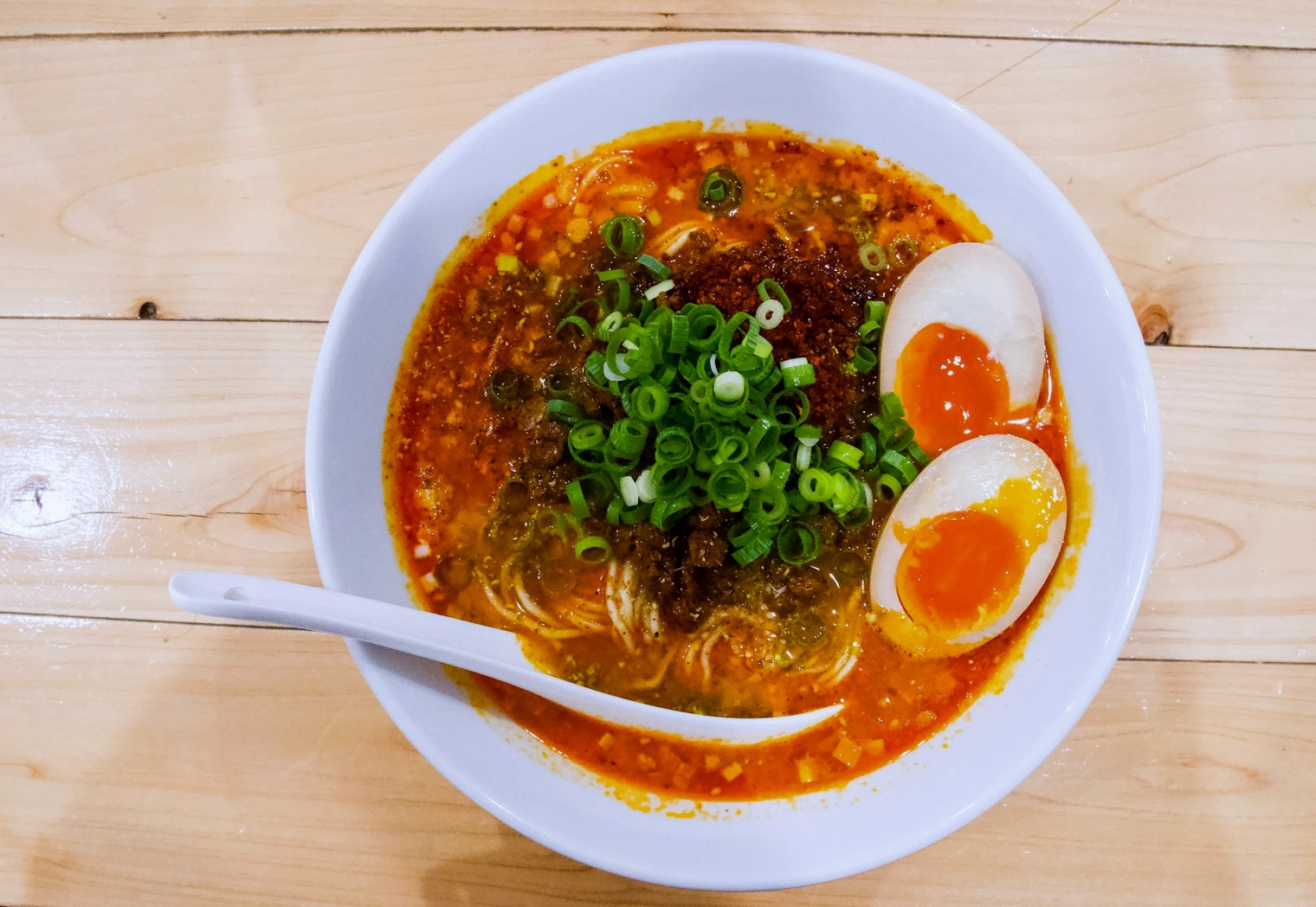 Spicy tantan ramen from above with red chili broth, scallions and two soft eggs