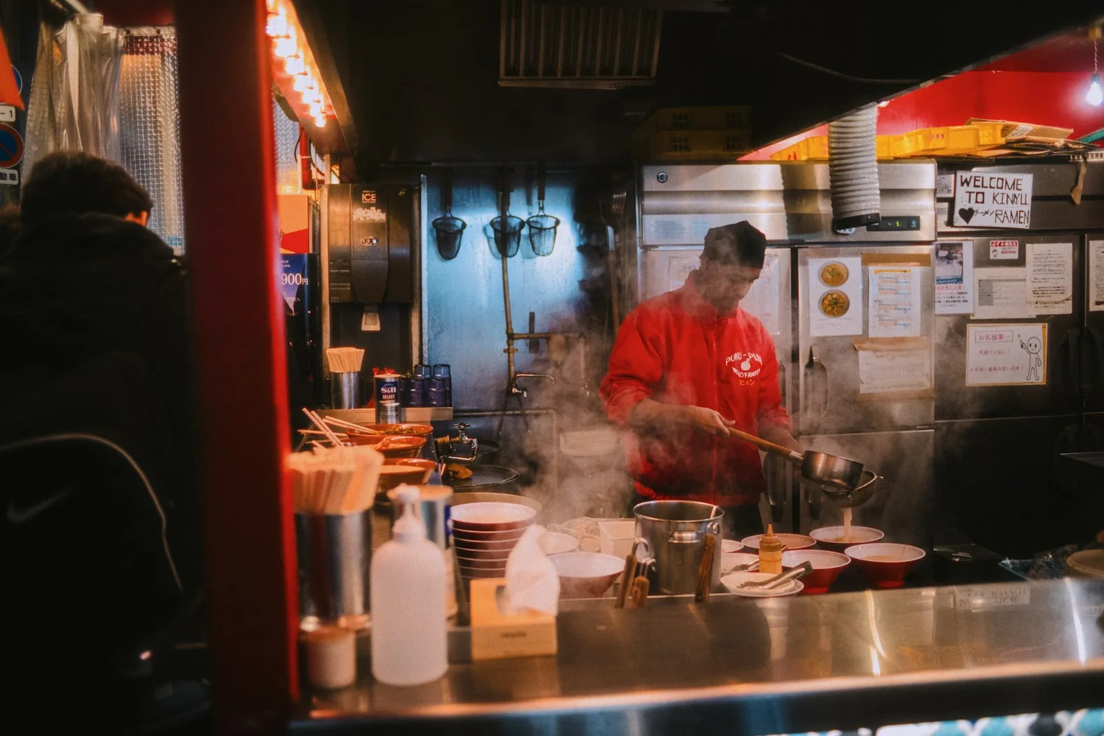 A cook working in a steamy open ramen kitchen