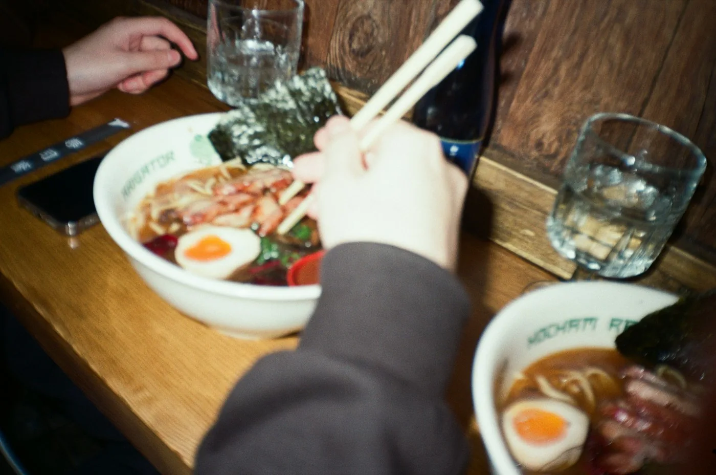A diner eating ramen with chopsticks at a wooden table