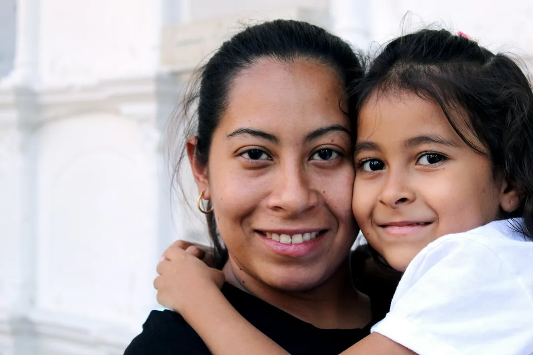 Mother and young daughter hugging cheek to cheek and smiling