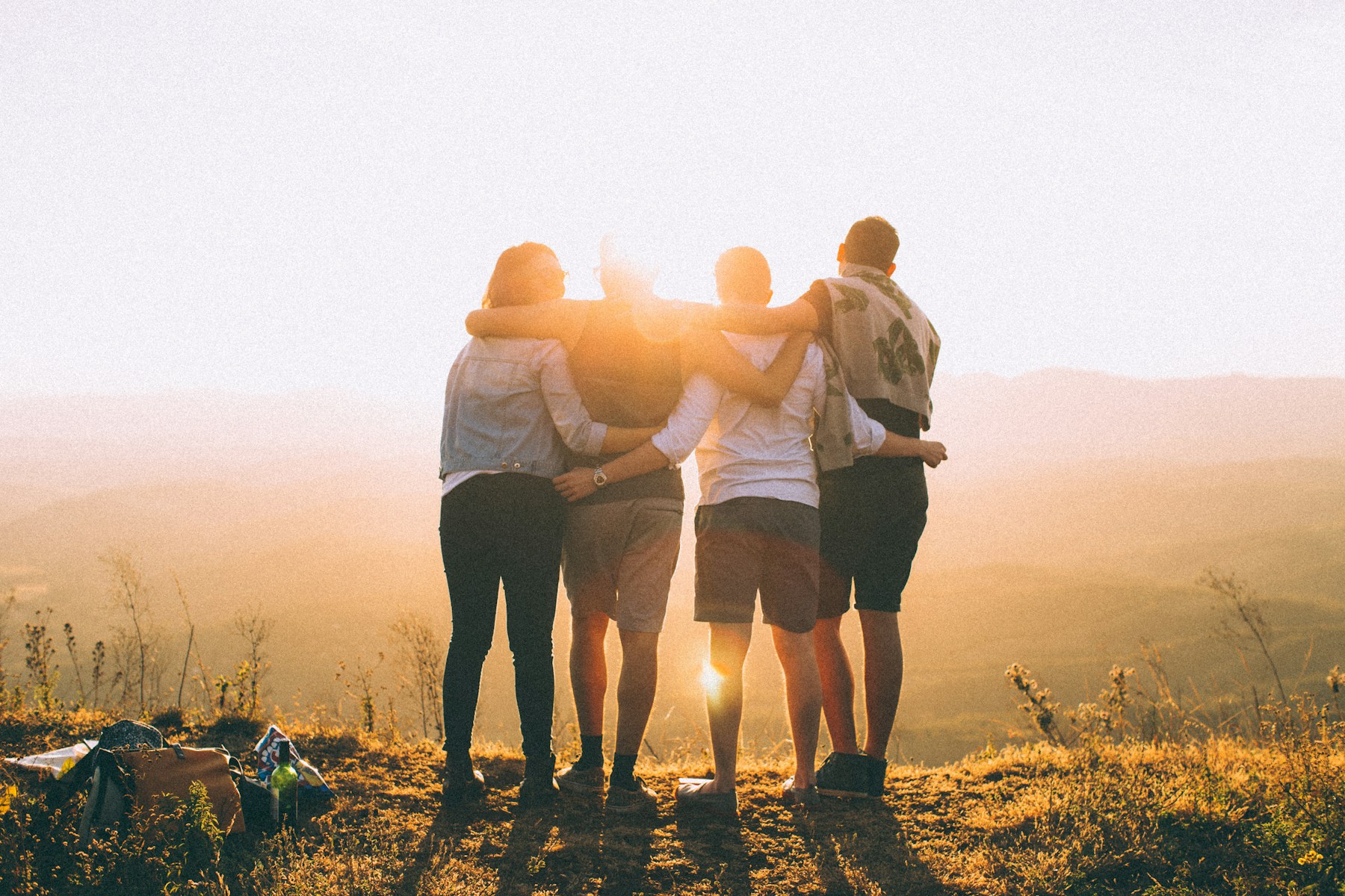 Four people with their arms around one another, looking toward a sunlit horizon