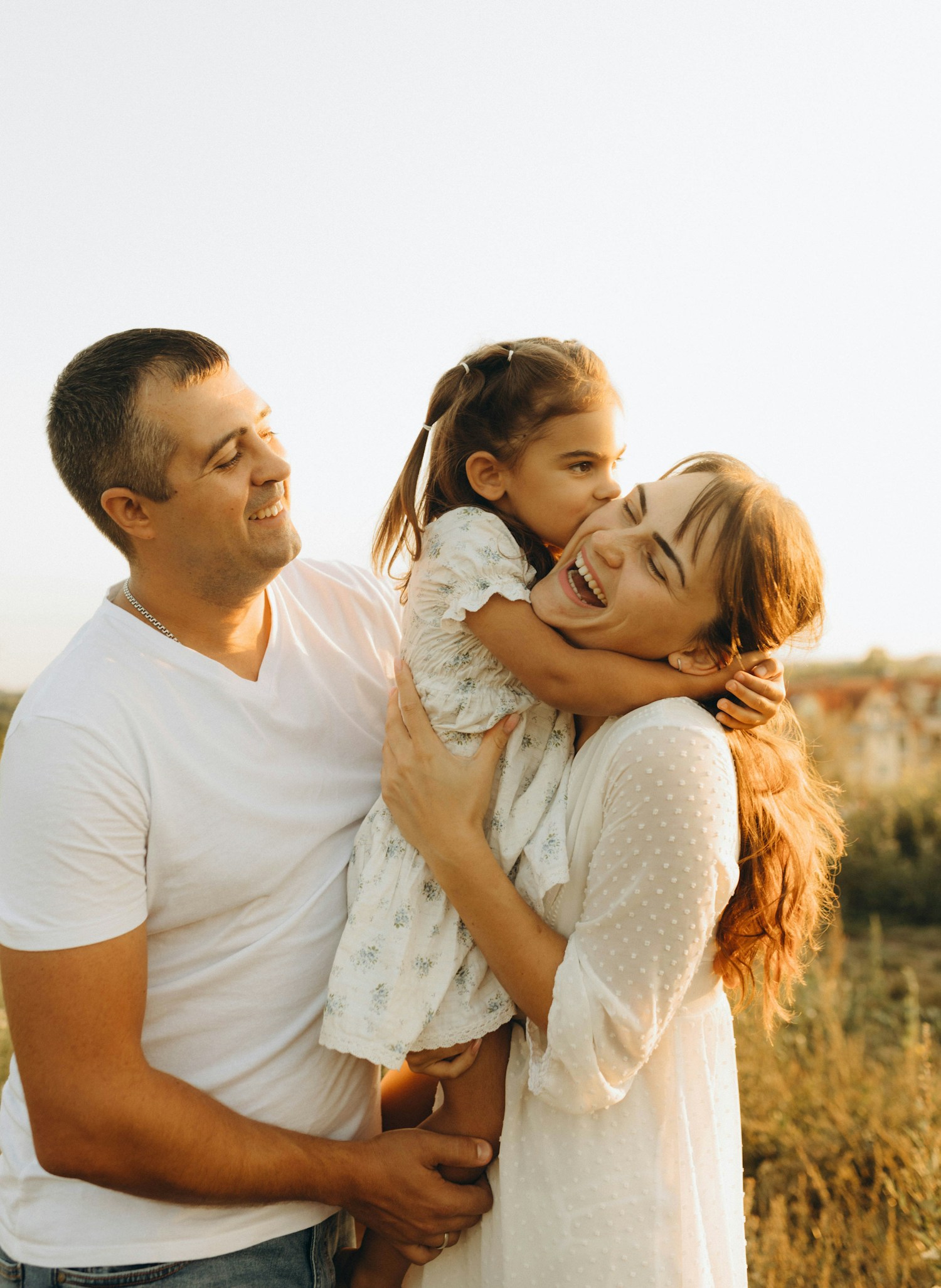 A mother and father sharing a joyful moment with their daughter in the afternoon sunshine