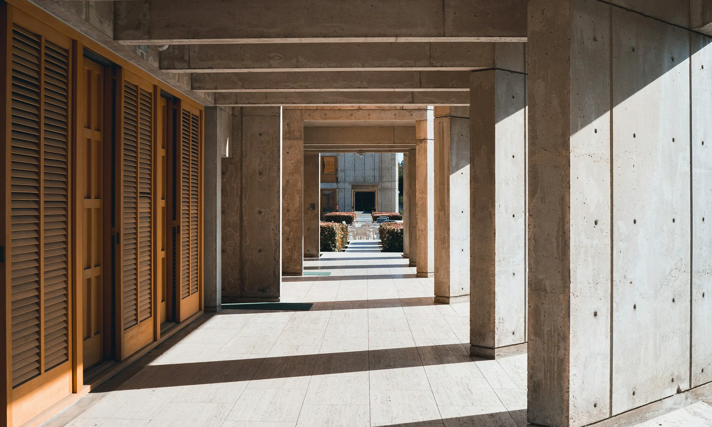 A timber-screened colonnade in afternoon light, concrete columns casting long shadows