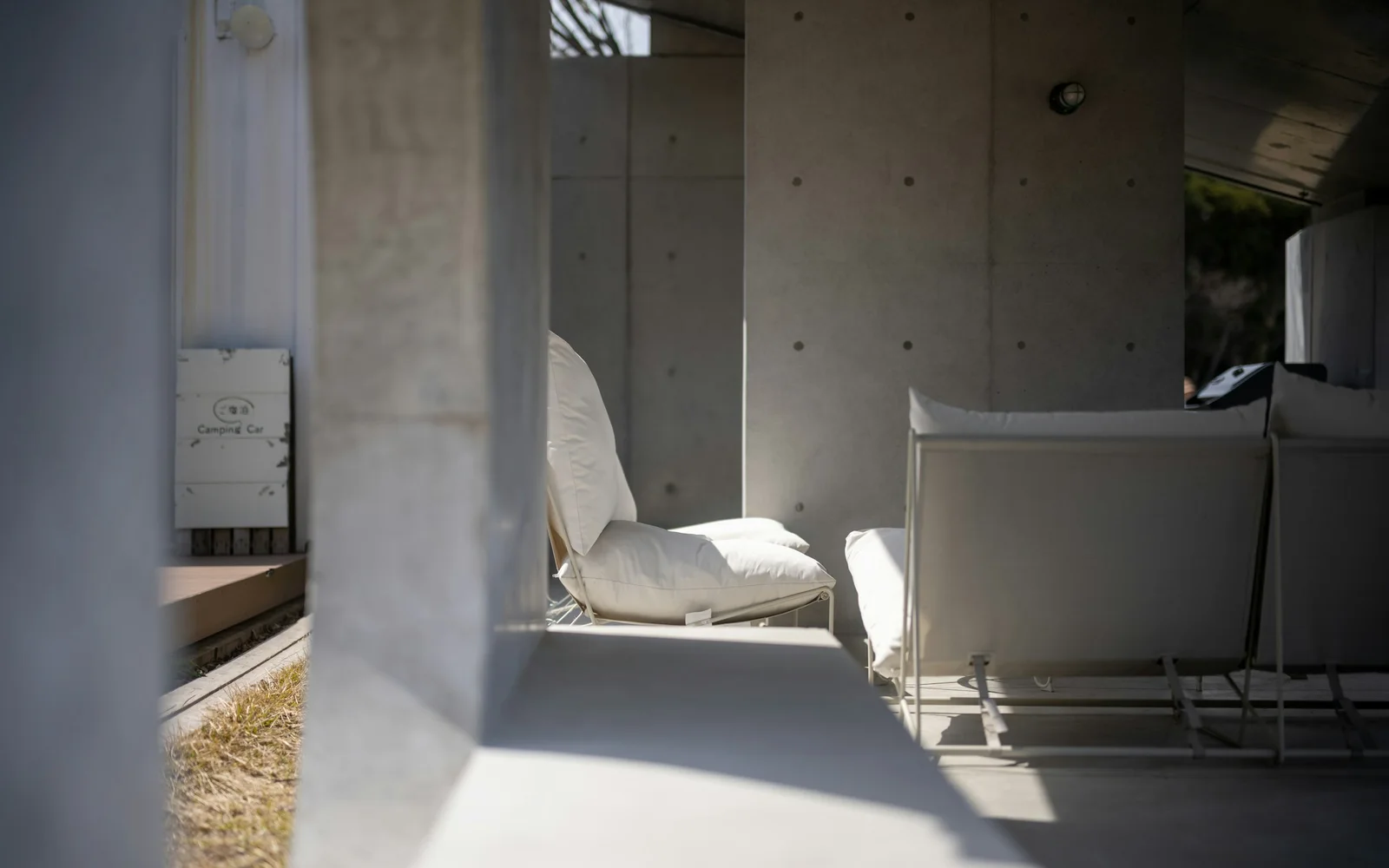 A quiet bedroom in a concrete and timber house, morning light across the wall