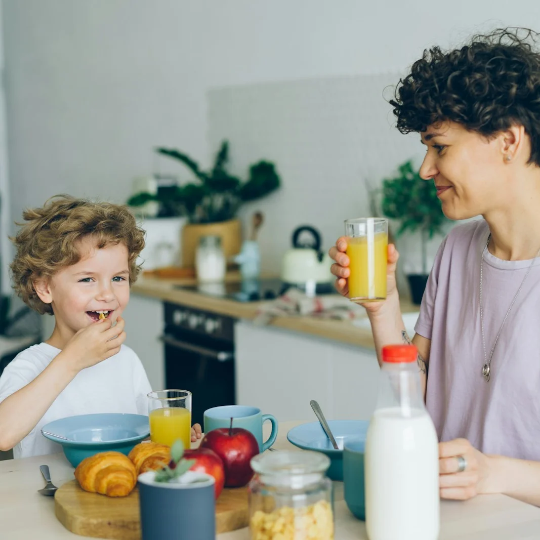 A mother and her young son laughing over breakfast in a bright kitchen