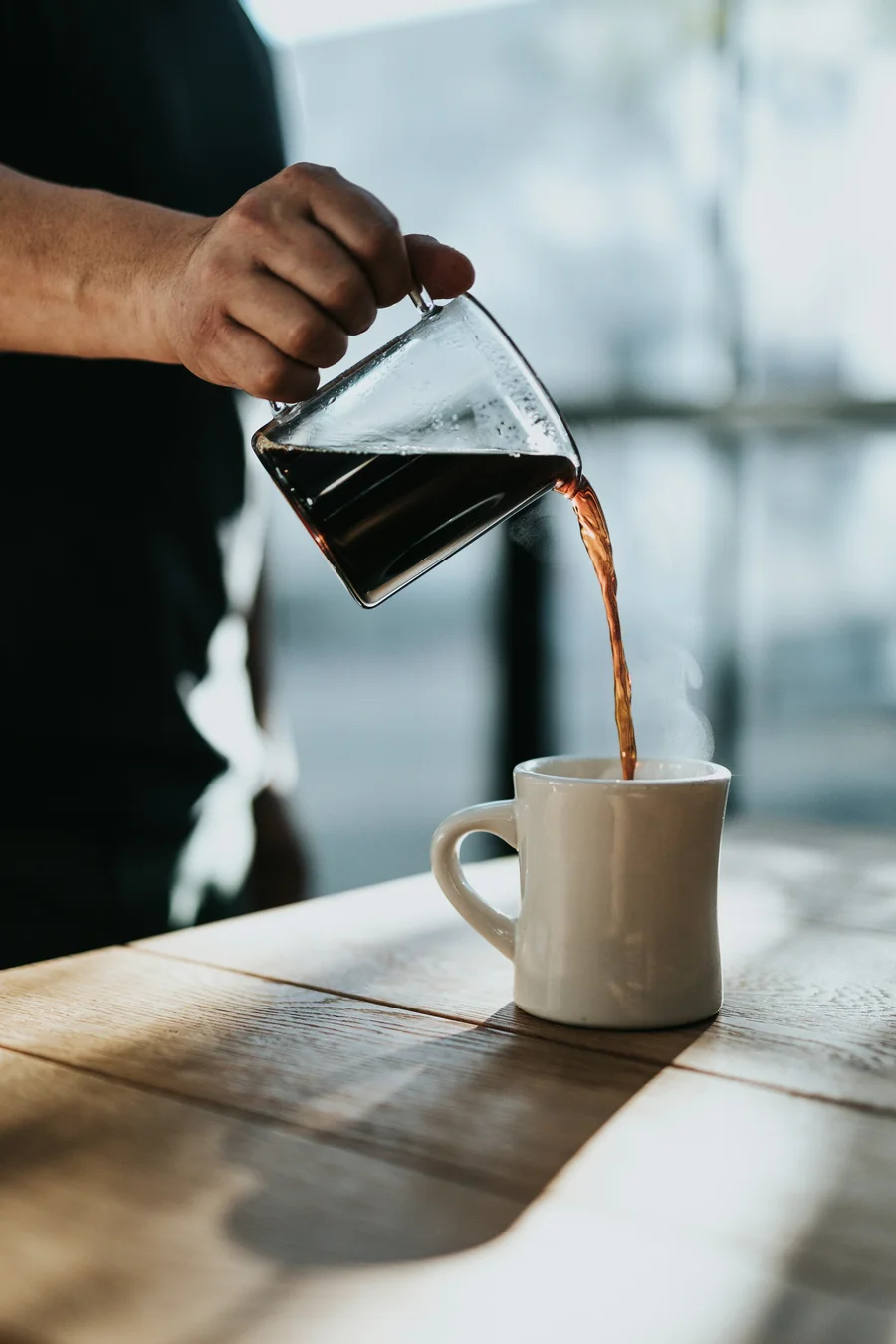 Black filter coffee poured from a glass jug into a white mug