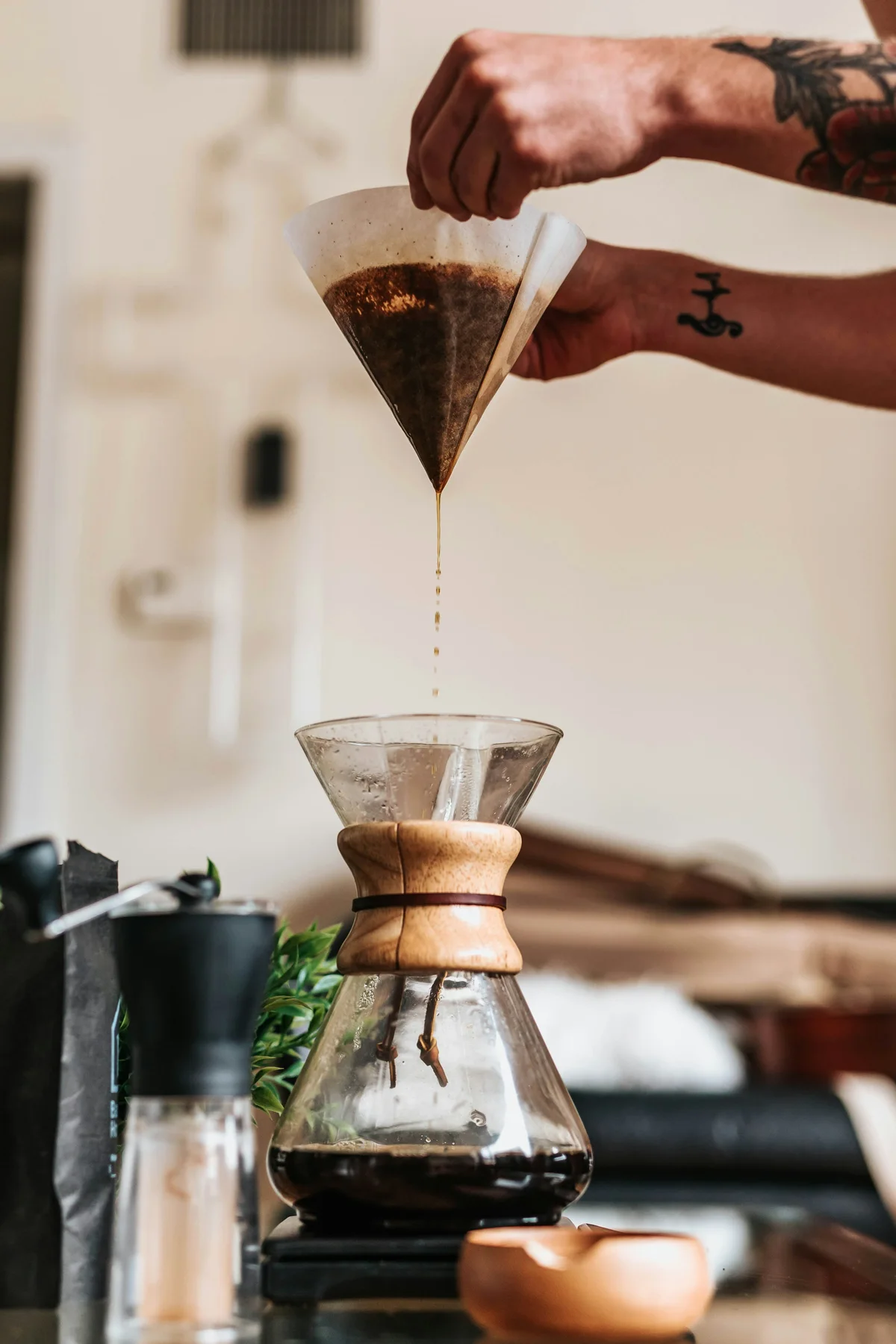 A barista pours filter coffee through a paper cone into a glass carafe