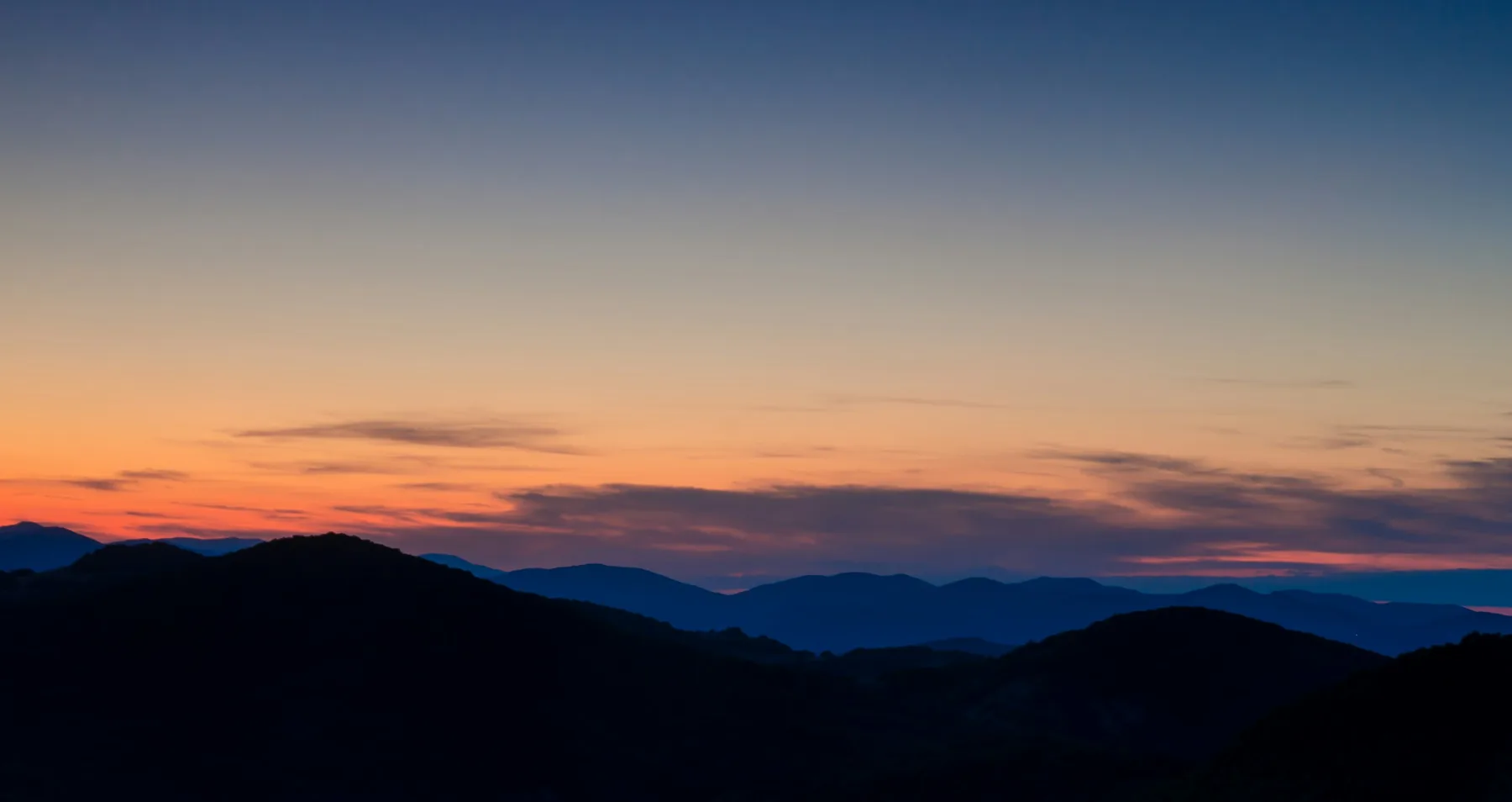 Dark ridges under a sky with a thin orange band of dawn