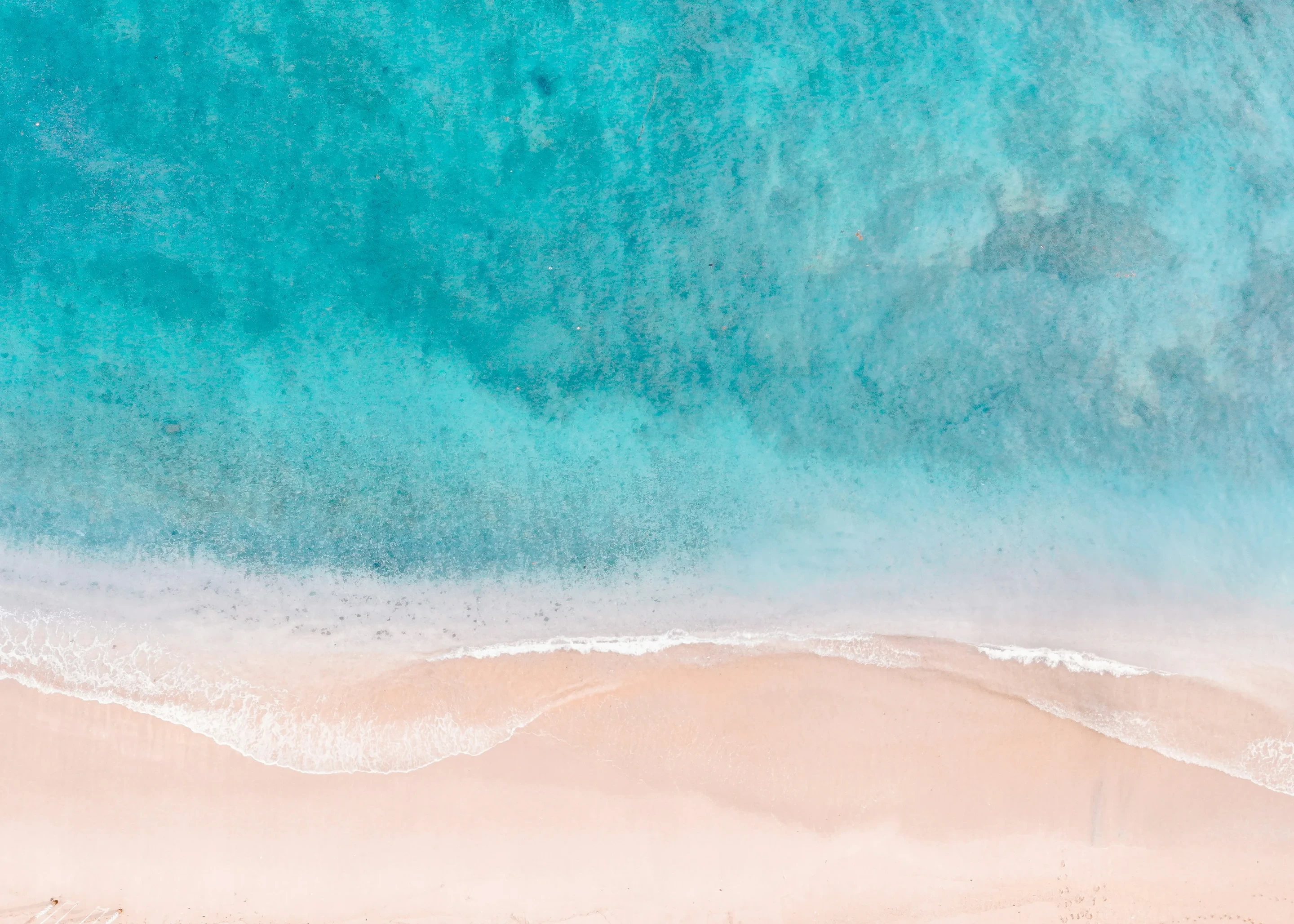 Pale sand meeting clear turquoise shallows, seen from above