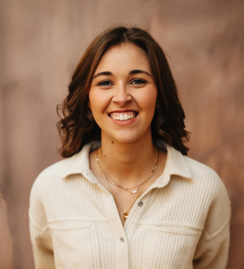 A smiling young woman in a cream shirt against a warm studio wall