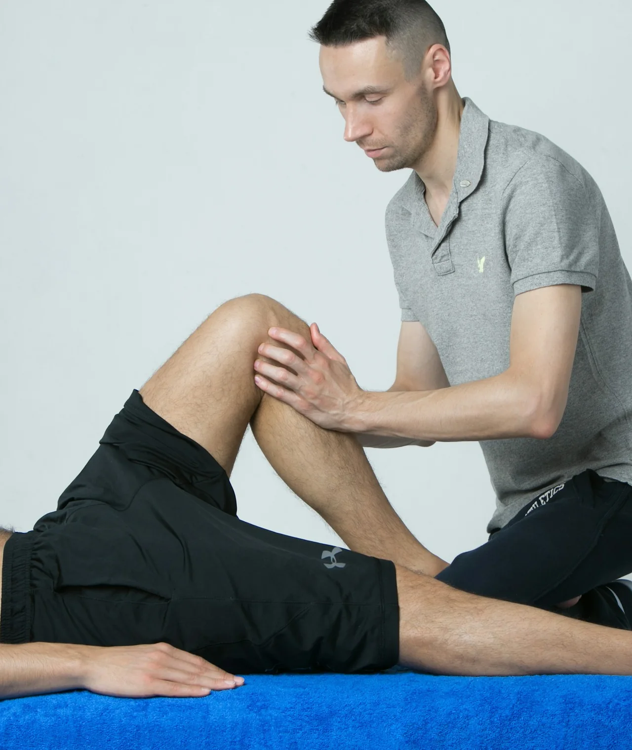 A physiotherapist testing a patient's bent knee on a treatment table in a bright room