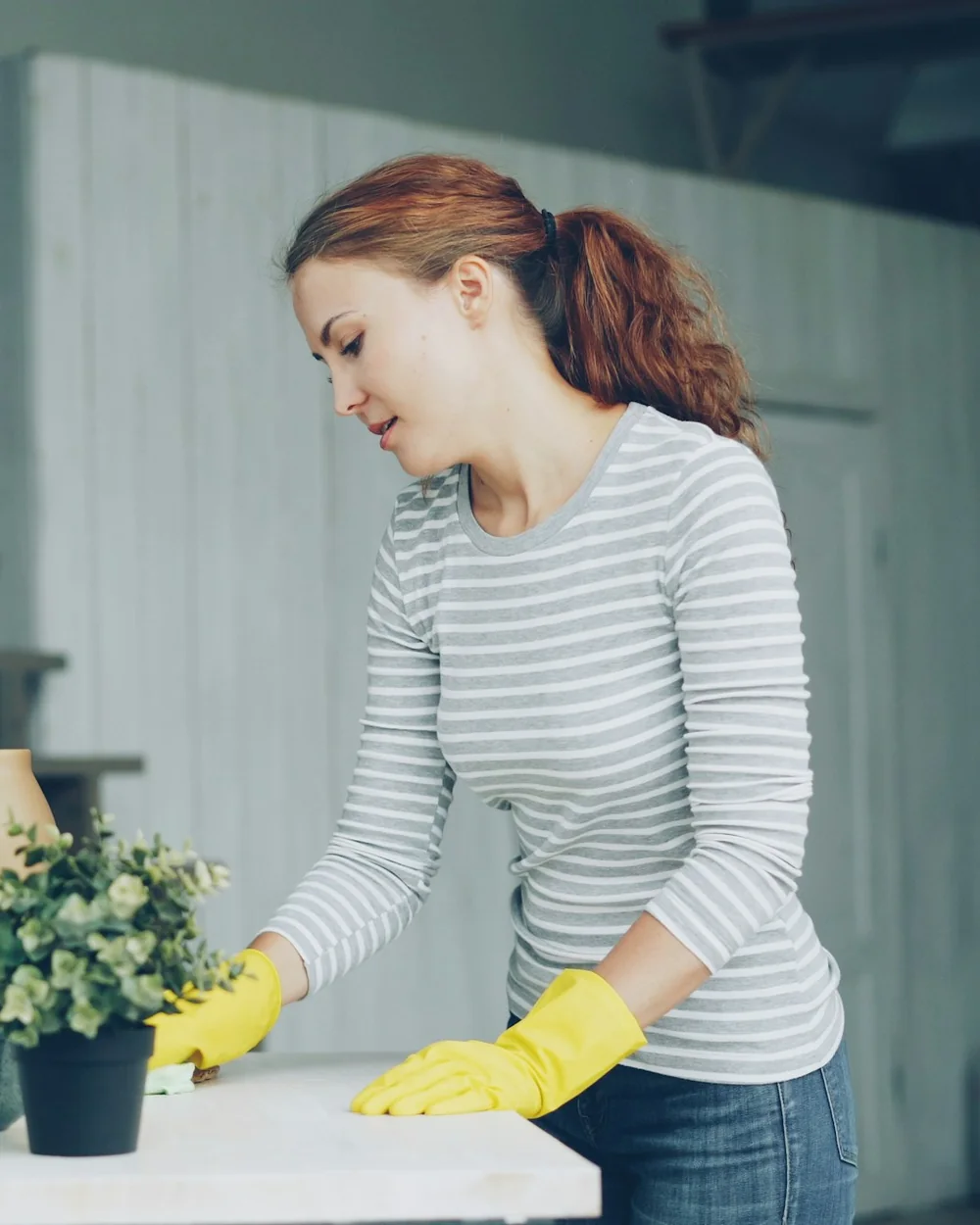Tidyhaus cleaner in yellow gloves wiping a white table by a window