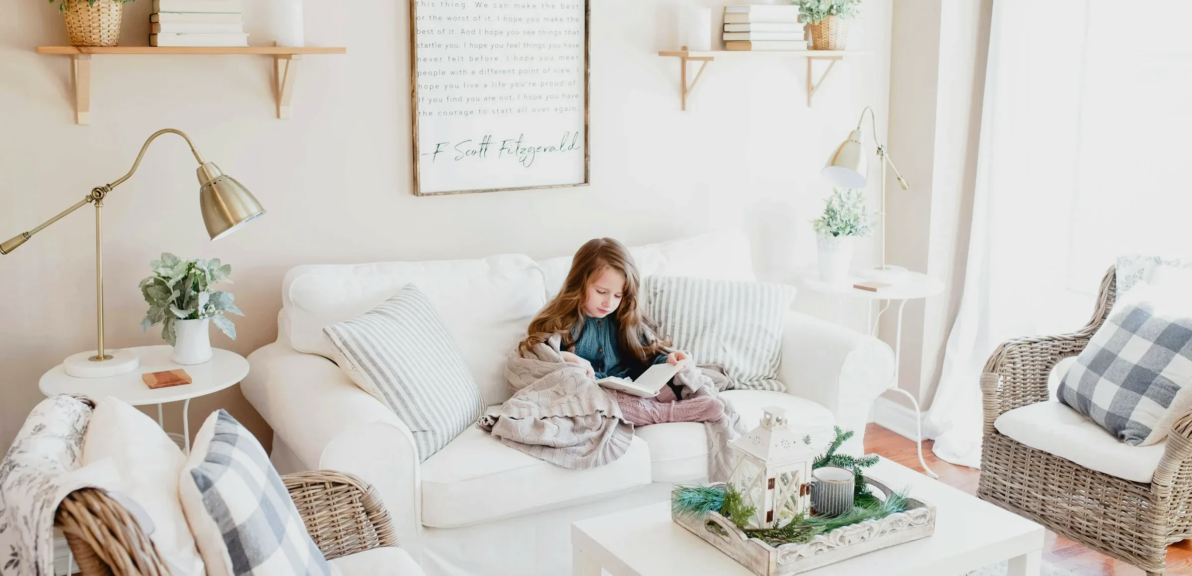 Girl reading under a blanket on a white sofa in a bright, tidy living room