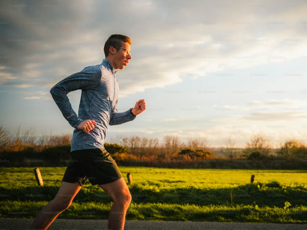 A runner in a grey top running past green fields at golden hour