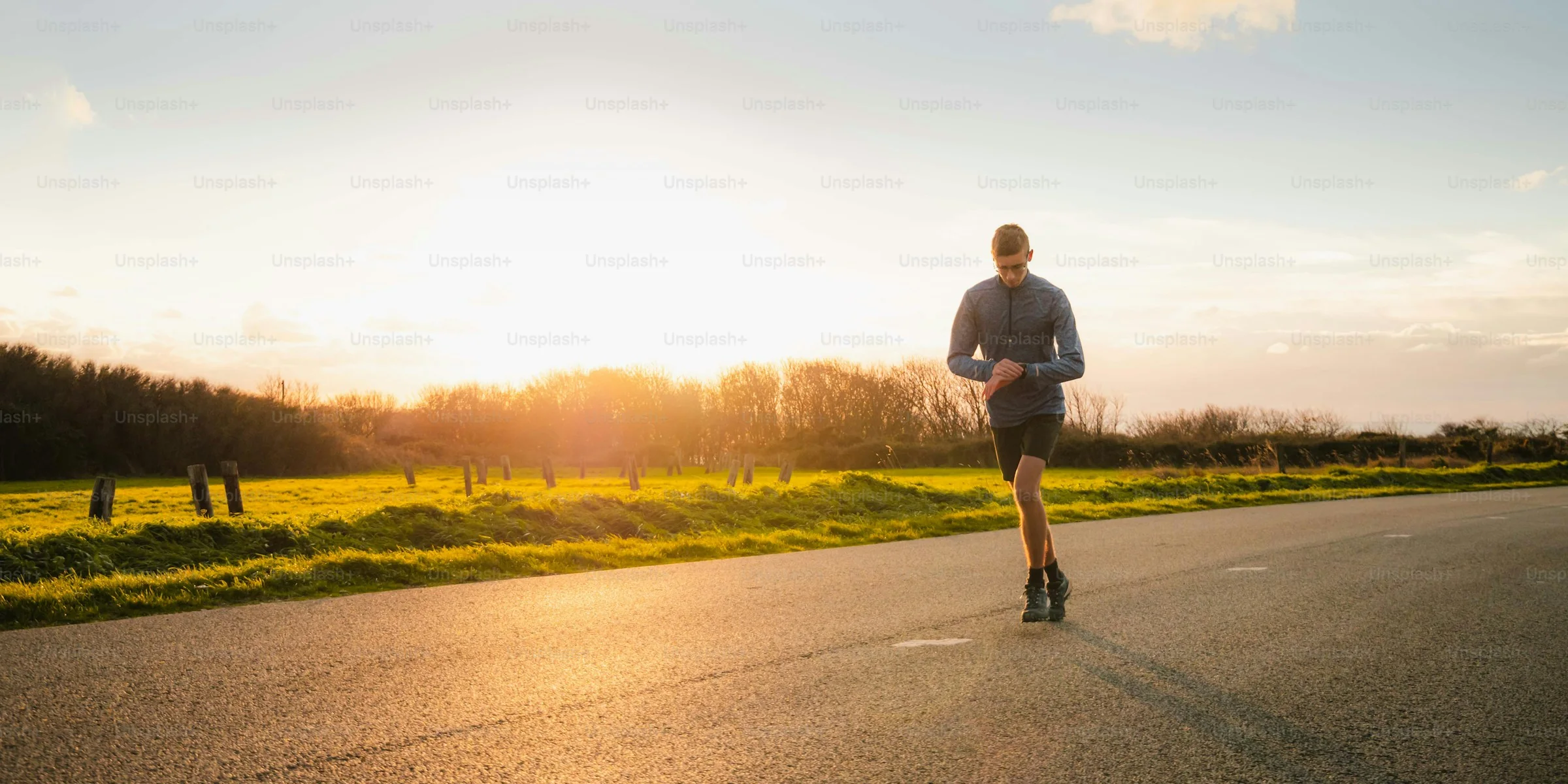 A runner checking his watch on an open road at sunset