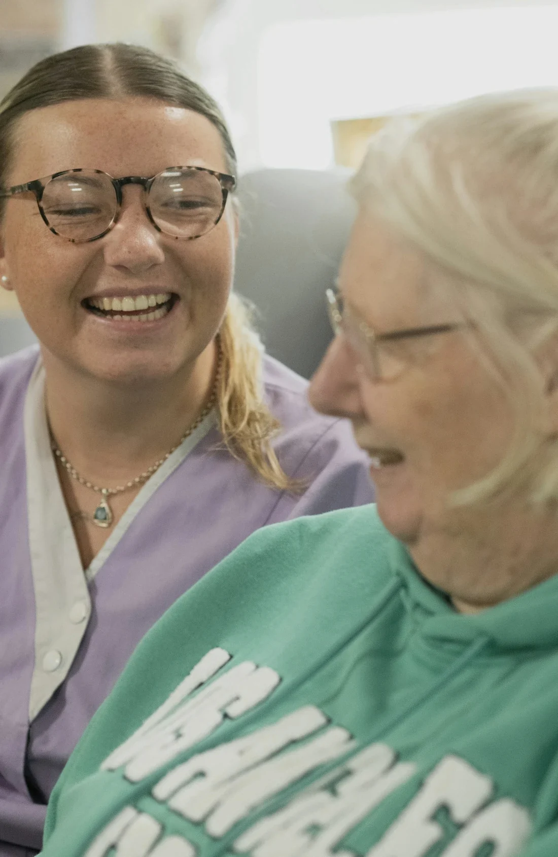 Carer in a lilac tunic laughing with an older resident