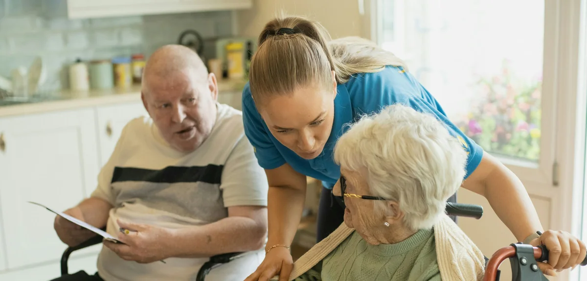Carer leaning in to help two residents with a colouring activity