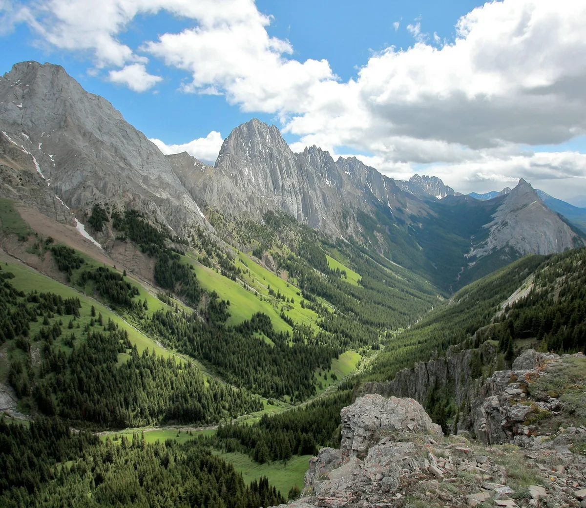 Grey limestone peaks above a green valley under white clouds on a bright day