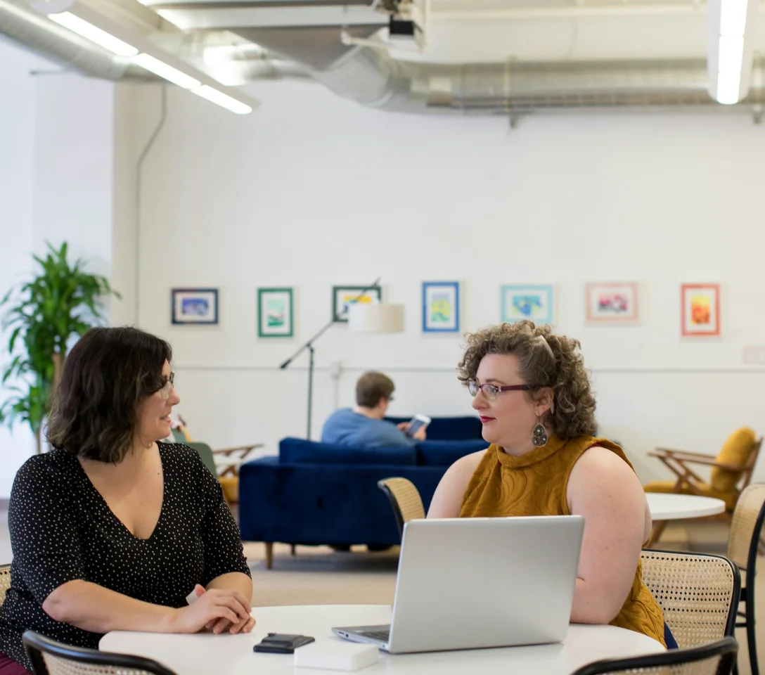 Two colleagues talking through their workflow at a round table with a laptop